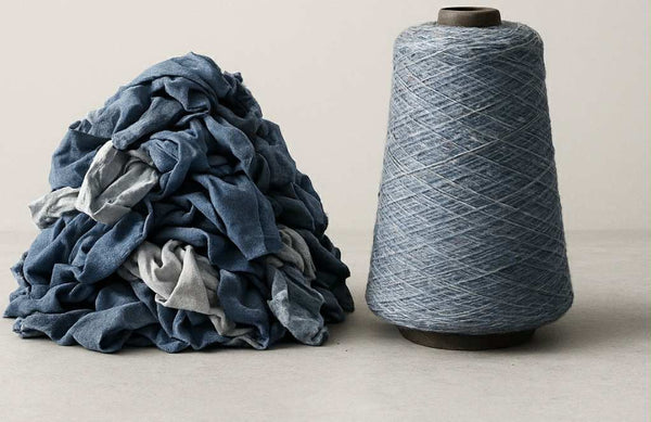Pile of blue and gray fabric next to a large spool of blue yarn on a beige background